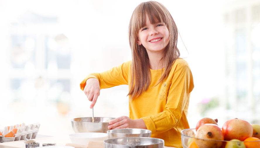 Child in a yellow shirt smiling with a mixing bowl