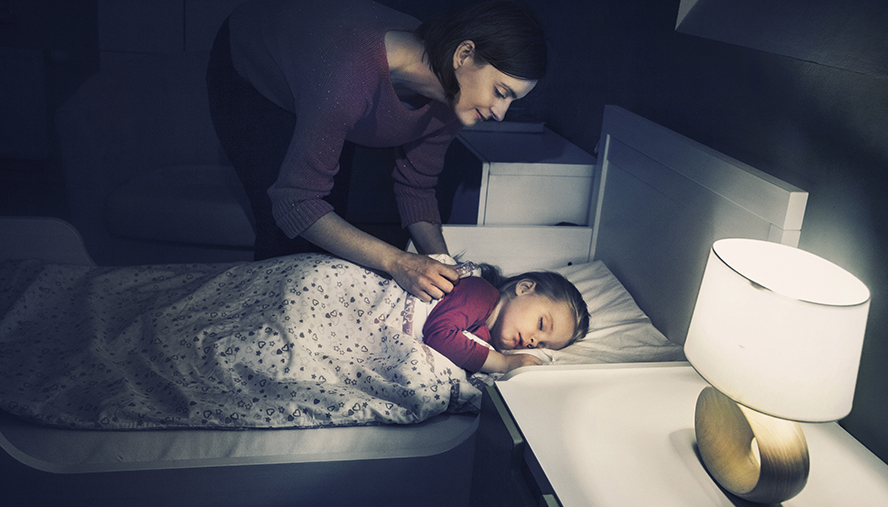 Mother tucking child in in a dark room with nightlight.