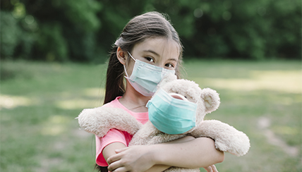 girl with facemask holding teddy bear